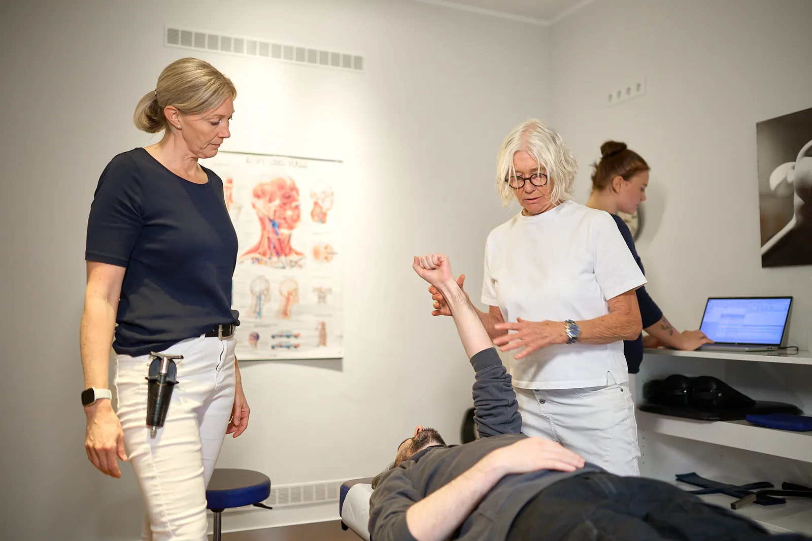 Zwei Behandlerinnen prüfen die Schulterbeweglichkeit eines Patienten in der Praxis Dr. Thiele